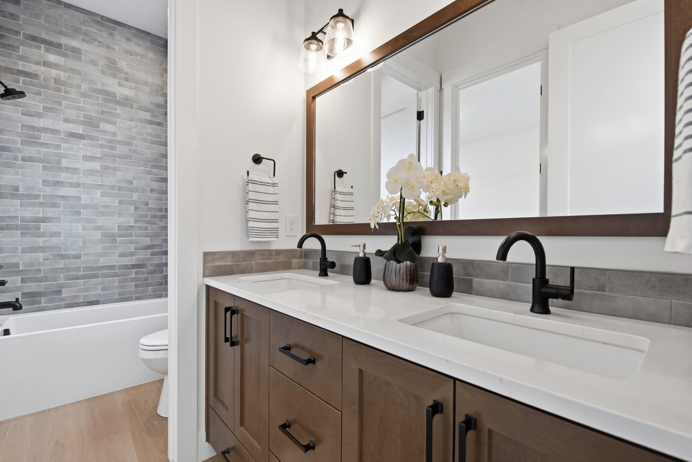 Double vanity with walnut cabinetry, black fixtures, and a full-width wood-framed mirror